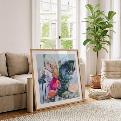 Framed abstract art in a living room with a couch, plant, and books.
