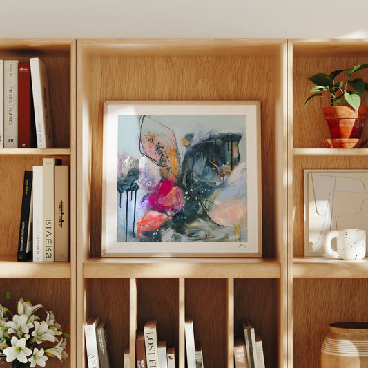 Framed abstract art on a wooden bookshelf with books and decorative items.