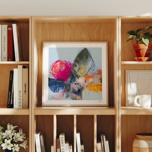 Framed abstract art on a wooden bookshelf with books and decorative items.