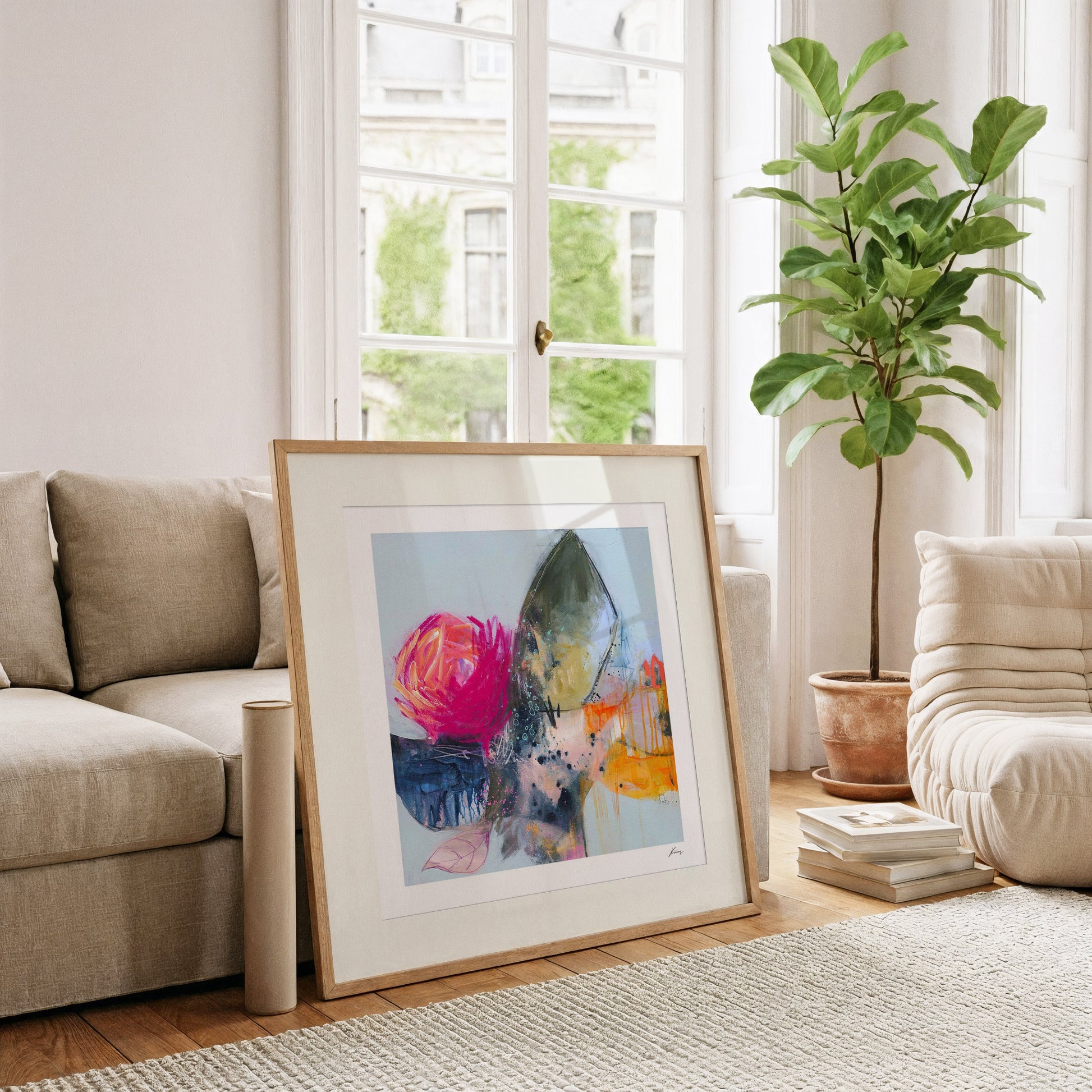 Framed abstract art piece on a coffee table in a living room with a couch and plant.