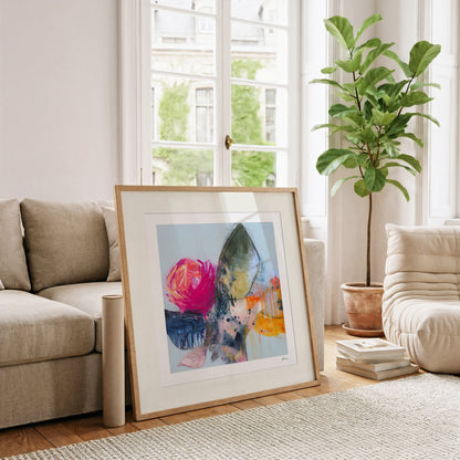 Framed abstract art piece on a coffee table in a living room with a couch and plant.