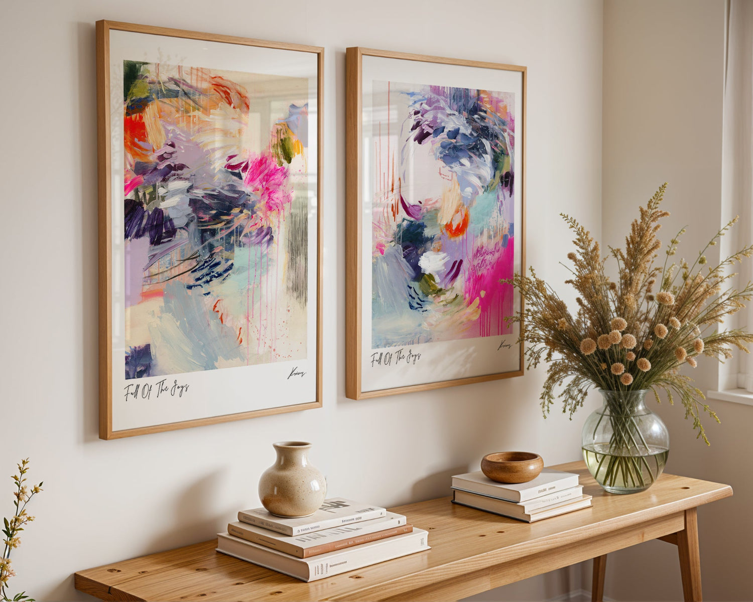 Two abstract art pieces on a wall above a wooden console table with decorative items.