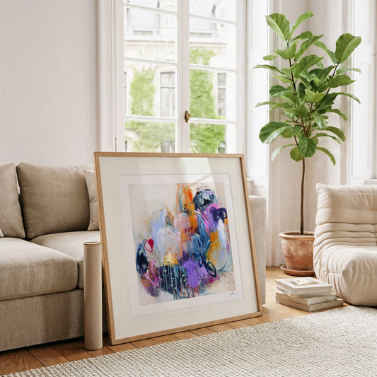 Framed abstract art in a living room with a couch, plant, and books.